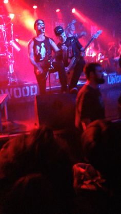 the band is performing on stage in front of an audience at a rock concert with red and purple lighting