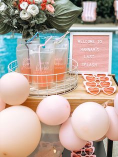 a table with balloons, drinks and signs on it next to a blue swimming pool