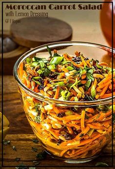 a glass bowl filled with carrot salad on top of a wooden table next to sliced lemons