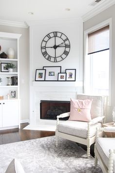 a living room with white furniture and a large clock on the wall above the fireplace