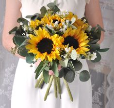 a bride holding a bouquet of sunflowers and greenery