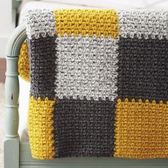 a crocheted blanket with yellow, gray and white squares