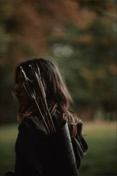 a woman with long hair holding two arrows in her hand and looking off into the distance