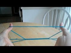 two hands are holding blue yarn over a wooden table with a white chair in the background