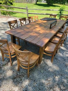 a wooden table with chairs around it in gravel area next to fence and grass field