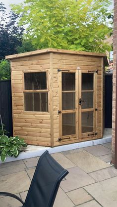 a wooden shed sitting on top of a patio next to a black chair and tree