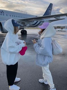 two women standing in front of an airplane on the tarmac talking to each other