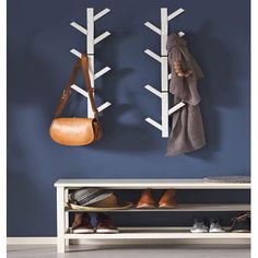 two white coat racks are hanging on the wall next to a bench with shoes and purses