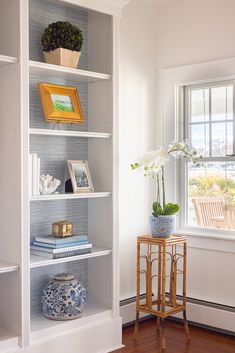 a white bookcase filled with lots of books next to a window and vase full of flowers