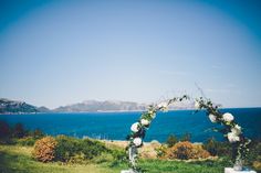 an outdoor ceremony setup with white flowers and greenery on the grass by the ocean