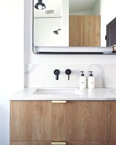 a bathroom vanity with white marble counter top and wooden cabinetry, along with two black faucets