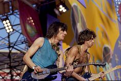 the rolling stones performing on stage at an outdoor concert in front of a colorful backdrop