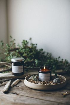 two candles sitting on top of a wooden table next to some rocks and greenery