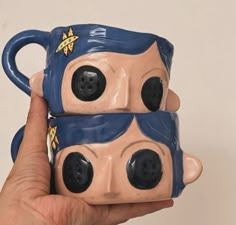 two coffee mugs with faces on them are being held by a person's hand