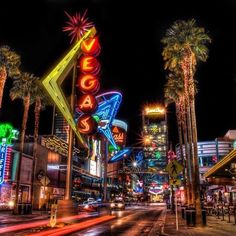 the las vegas sign lit up at night with palm trees and buildings in the background