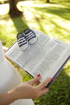 a pregnant woman holding an open book with shoes on her belly and reading it in the grass