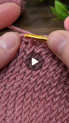 someone is crocheting the stitchs on a pink knitted sweater with a golden needle