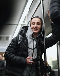 a woman standing on a bus holding onto a pole with one hand and smiling at the camera