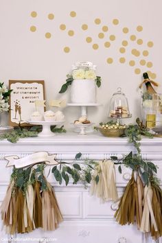 a table topped with cake and cupcakes on top of a white mantle covered in greenery