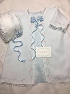 a baby's blue and white outfit is laying on top of a sheet with a name tag