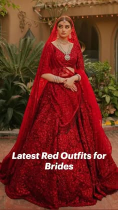 a woman in a red wedding gown standing on a brick floor with greenery behind her