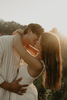 a man and woman kissing in front of the sun with their arms around each other