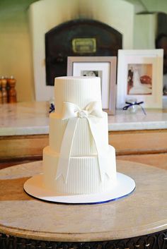 a three tiered white wedding cake with a bow on the top, sitting on a table