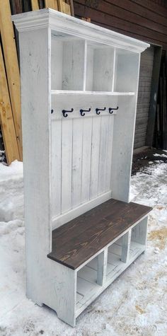 a white wooden bench sitting in the middle of snow covered ground with two coat hooks on it's back