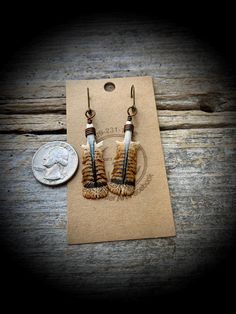 two brown and white earrings sitting on top of a piece of paper next to a penny