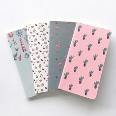 four notebooks with cactus designs on them are lined up against a white background, one is pink and the other is blue