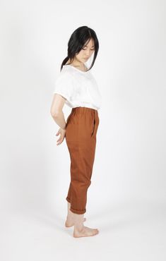 a woman standing in front of a white background wearing brown pants and a white shirt