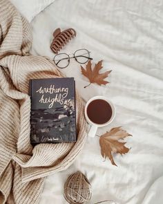 a book sitting on top of a bed next to a cup of coffee and yarn