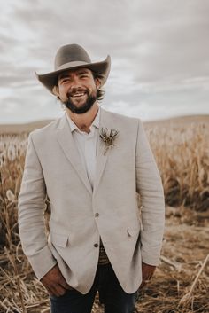 a man with a beard wearing a cowboy hat standing in the middle of a field