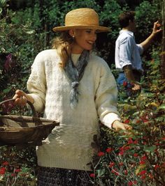 a woman wearing a straw hat and holding a basket in her hand while standing next to flowers