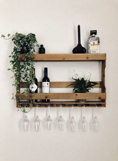 a wooden shelf with wine glasses and bottles on it next to a potted plant