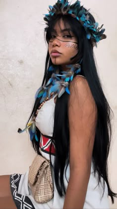 a woman with long black hair and blue feathers on her head is posing for the camera