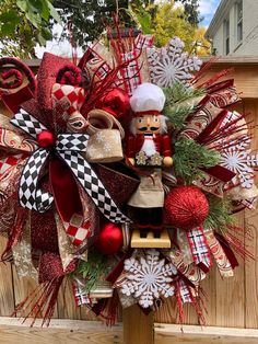 a christmas wreath with red and white decorations hanging on the side of a wooden fence