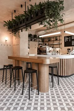 the interior of a coffee shop with plants hanging from the ceiling and bar stools