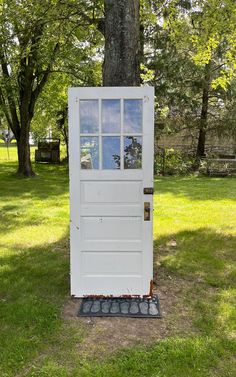 a white door sitting in the grass next to a tree