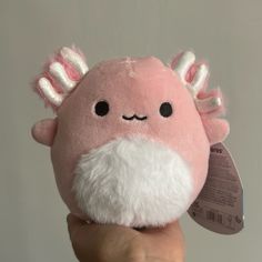 a hand holding a pink stuffed animal with white hair and horns on it's head