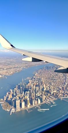 the wing of an airplane flying over a large body of water in front of a city