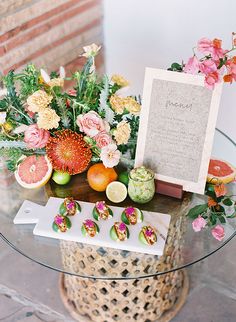 a glass table topped with fruit and flowers next to a sign that says thank you