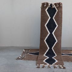 a brown and black rug with tassels on the floor next to a white wall