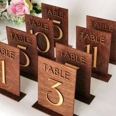 wooden table numbers are displayed with flowers in the background