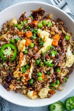 a white bowl filled with rice, meat and veggies next to green peppers