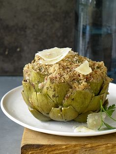 a white plate topped with artichoke covered in cheese and herbs next to a vase