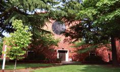 the building is surrounded by trees and grass, with a clock on it's face