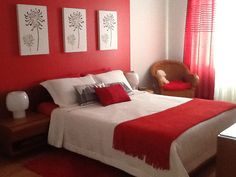 a bedroom with red walls and white bedding in the corner, along with two paintings on the wall