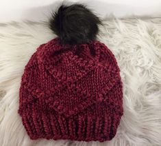 a red knitted hat with a black pom - pom on the top