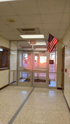 an empty hallway with american flag hanging from the ceiling and glass doors on both sides